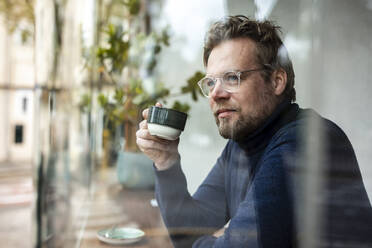 Contemplative businessman having coffee in cafe seen through glass window - JOSEF11063