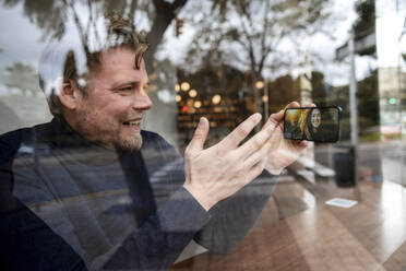 Lächelnder Geschäftsmann führt einen Videoanruf mit seiner Freundin auf einem Smartphone in einem Café - JOSEF11067