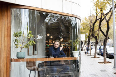 Businessman holding credit card in cafe seen through glass window - JOSEF11069