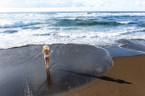 Luftaufnahme einer Frau im Bikini am Strand, die ihre Sonnenbrille hält, Sao Miguel, Azoren, Portugal. - AAEF14938