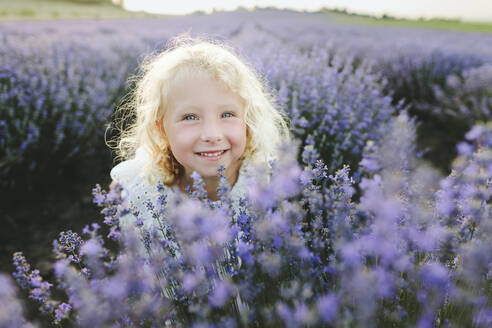 Lächelndes Mädchen mit blondem Haar inmitten von Lavendelpflanzen - SIF00257
