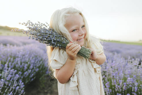 Lächelndes Mädchen mit Lavendelbouquet im Feld stehend - SIF00260