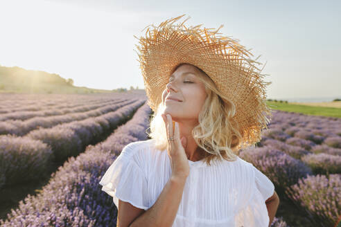 Smiling woman with eyes closed touching chin in lavender field - SIF00263