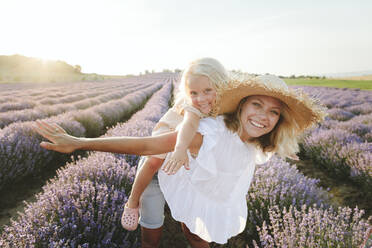 Happy woman giving piggyback ride to daughter in lavender field - SIF00269