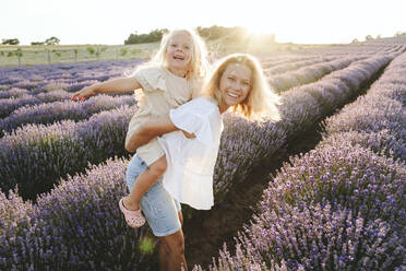 Happy girl enjoying piggyback ride on mother in lavender field - SIF00271