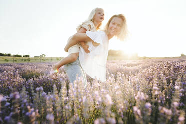 Happy mother giving piggyback ride to daughter in field - SIF00272