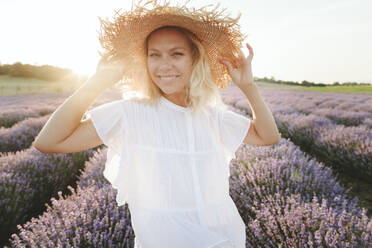 Smiling woman wearing straw hat standing in lavender field - SIF00279