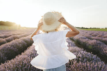 Woman wearing straw hat standing in lavender field - SIF00280