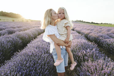 Mother kissing daughter in lavender field at sunset - SIF00289