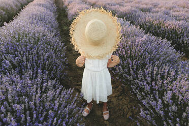 Girl hiding face with hat standing in lavender field - SIF00290