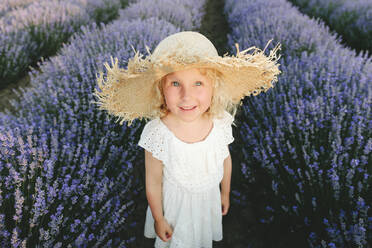 Lächelndes süßes Mädchen mit Strohhut in einem Lavendelfeld stehend - SIF00291
