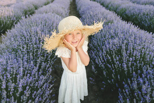 Glückliches süßes Mädchen, das inmitten von Lavendelpflanzen steht - SIF00292
