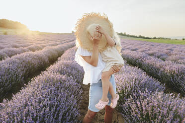 Mother and daughter covering face with hat in lavender field - SIF00293