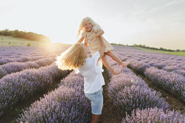 Playful mother enjoying with daughter in lavender field - SIF00298