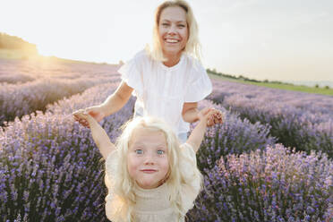 Glückliche Mutter spielt mit Tochter in Lavendelfeld bei Sonnenuntergang - SIF00300
