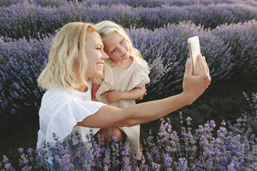 Happy woman taking selfie with daughter through smart phone amidst lavender flowers - SIF00307