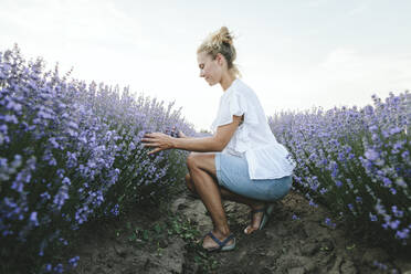 Lächelnde Frau berührt Lavendelblüten auf einem Feld - SIF00320