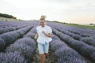 Glückliche Frau läuft inmitten von Lavendelpflanzen - SIF00323