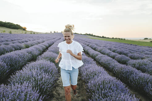 Happy woman running amidst lavender plants - SIF00323