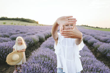 Frau schaut durch Fingerrahmen in Lavendelfeld - SIF00336