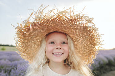 Happy girl wearing straw hat standing in lavender field - SIF00337