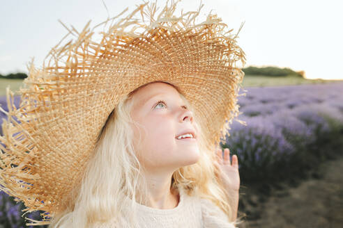 Lächelndes süßes Mädchen mit Hut in einem Lavendelfeld stehend - SIF00338