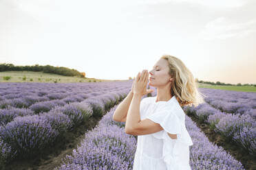 Smiling woman with hands clasped praying in lavender field - SIF00340