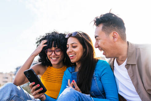 Von unten glücklich multiethnischen Mann und Frauen lächelnd und Surfen in den sozialen Medien auf Handys beim Ausruhen am Strand auf sonnigen Sommertag auf Resort - ADSF35649