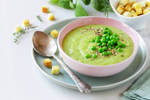 Köstliche gesunde Erbsencremesuppe in einer Schale, garniert mit grünen Erbsen und Croutons auf dem Tisch - ADSF35679