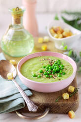 Delicious healthy cream pea soup in a bowl garnished with green peas and croutons on table - ADSF35680