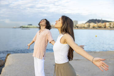 Young couple standing with arms outstretched and eyes closed at pier - WPEF06104