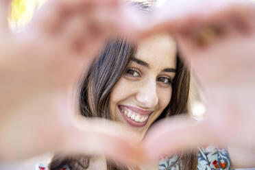 Smiling young woman making heart from hands - WPEF06139