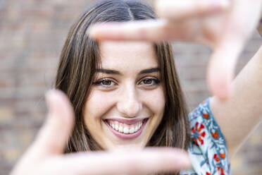 Smiling young woman making finger frame - WPEF06140