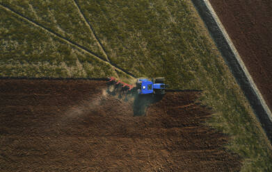 Aerial view of a tractor plowing a field by tilling the soil with a mechanized plow ahead of the sowing period in Lomellina, Po Valley, Italy. - AAEF14962