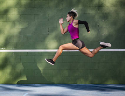 Athletic woman with prosthetic arm running against wall - TETF01656