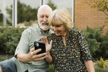 Lächelndes älteres Paar mit Videoanruf im Hinterhof - TETF01669