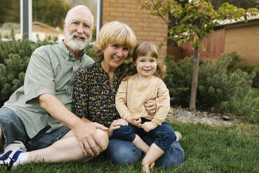 Portrait of smiling grandparents with granddaughter (4-5) on back yard - TETF01672