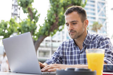 Älterer digitaler Nomade arbeitet am Laptop in einem Café im Freien - WPEF06160