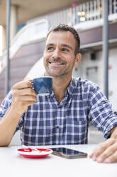 Lächelnder reifer Mann trinkt Kaffee in einem Straßenkaffee - WPEF06173