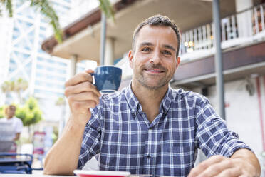Smiling man with cup of coffee sitting at outdoor cafe - WPEF06174