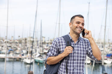 Lächelnder reifer Mann, der am Hafen mit seinem Smartphone telefoniert - WPEF06177