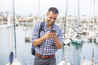Glücklicher reifer Mann, der ein Mobiltelefon im Hafen benutzt - WPEF06178