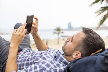 Älterer Mann mit Mobiltelefon entspannt am Strand - WPEF06184