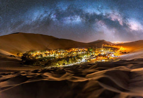 Magnificent Huacachina village and oasis with bright illumination located near sandy dunes of Atacama desert against starry night sky in Peru - ADSF35705