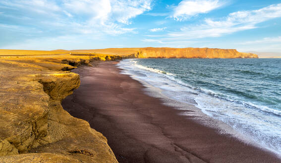 Spectacular landscape of powerful ocean with foamy waves rolling on sandy beach surrounded by rocky formations against bright cloudy blue sky in Paracas National Reserve in Peru - ADSF35720