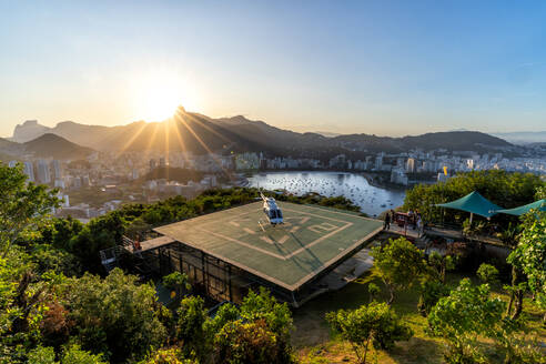 Moderne Hubschrauber Landung auf der Plattform von üppigen grünen Bäumen in der Nähe von Meer gegen wolkenlosen Sonnenuntergang Himmel in Rio de Janeiro umgeben - ADSF35723