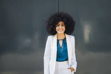 Smiling young Afro businesswoman standing in front of wall - MEUF06856