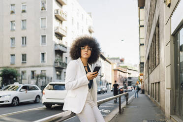 Businesswoman with mobile phone sitting on railing - MEUF06858