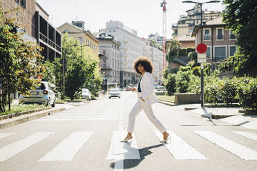 Young businesswoman crossing street on sunny day - MEUF06864