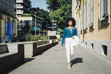 Businesswoman with laptop walking on sidewalk in city - MEUF06869